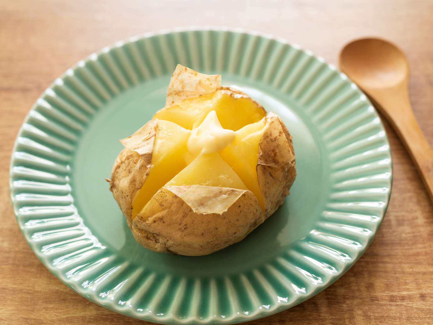 A green plate with a baked potato, topped with a click of butter
