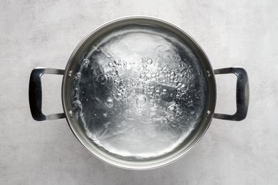 Overhead shot of a stainless steel metal cooking pot of boiling water on gray concrete background