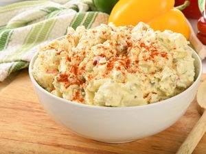 Bowl of sweet potato salad with paprika sprinkle placed on a wooden board
