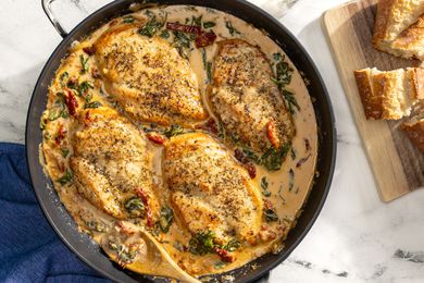 creamy tuscan chicken in a pot next to sliced bread on a wooden board