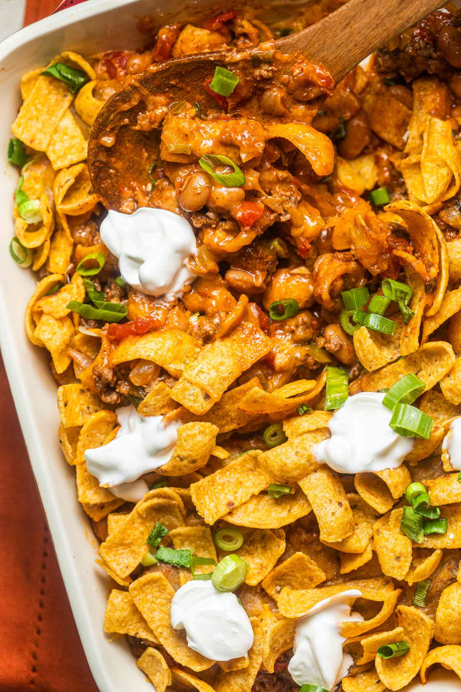 Walking taco casserole with dollops of sour cream in a casserole dish with a serving spoon (casserole dish missing some casserole)