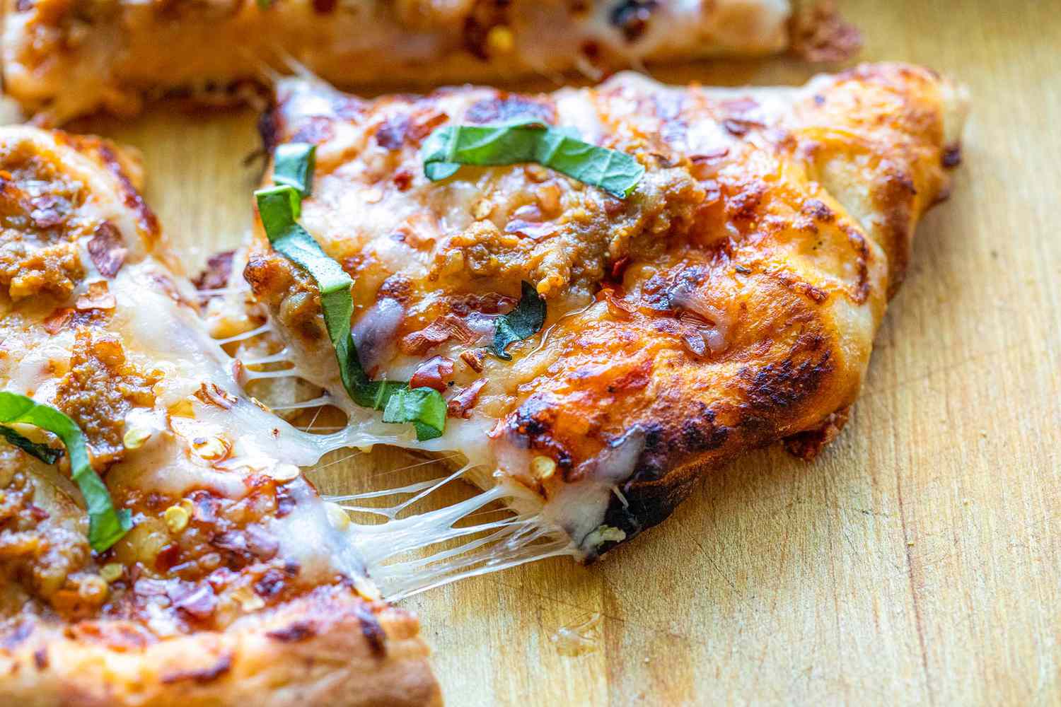 Sausage pizza, cooked in a Roccbox outdoor pizza, oven with a slice of stringy cheese connecting it to the rest of the pizza