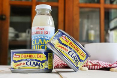 Two cans of clams and a bottle of clam juice on a table. Canned clams give 'em a try!