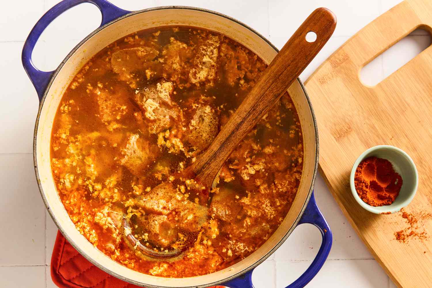 Sopa de Ajo in a large pot with pieces of toast and a wooden spoon, small bowl of paprika on the side