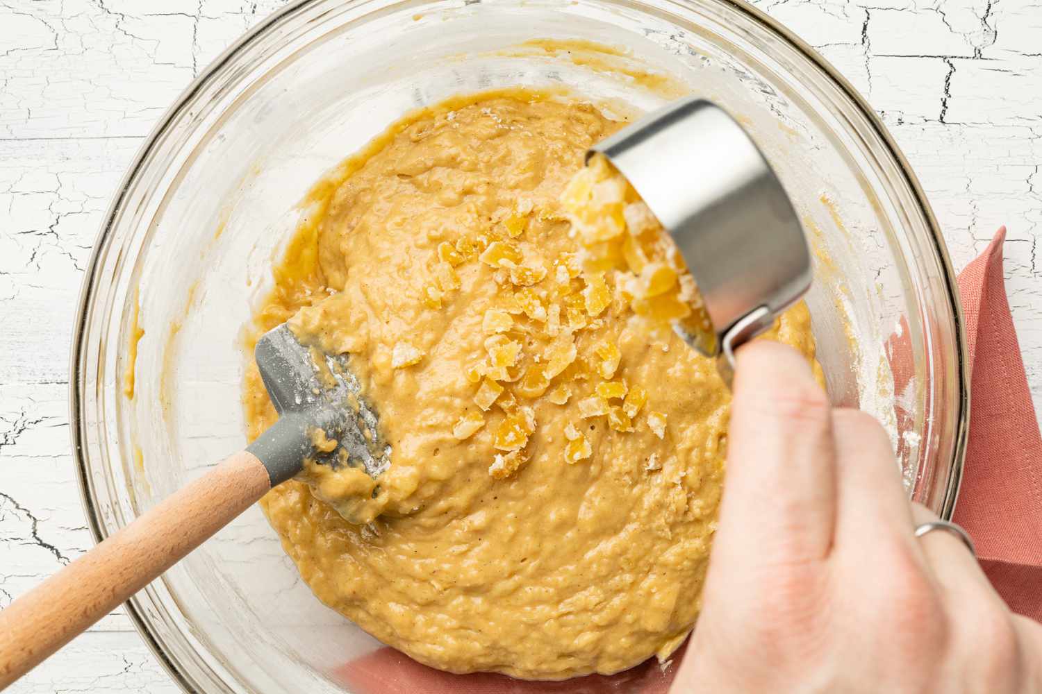 Measuring Cup of Candied Ginger Poured Into Bowl of Dark and Stormy Banana Bread Batter