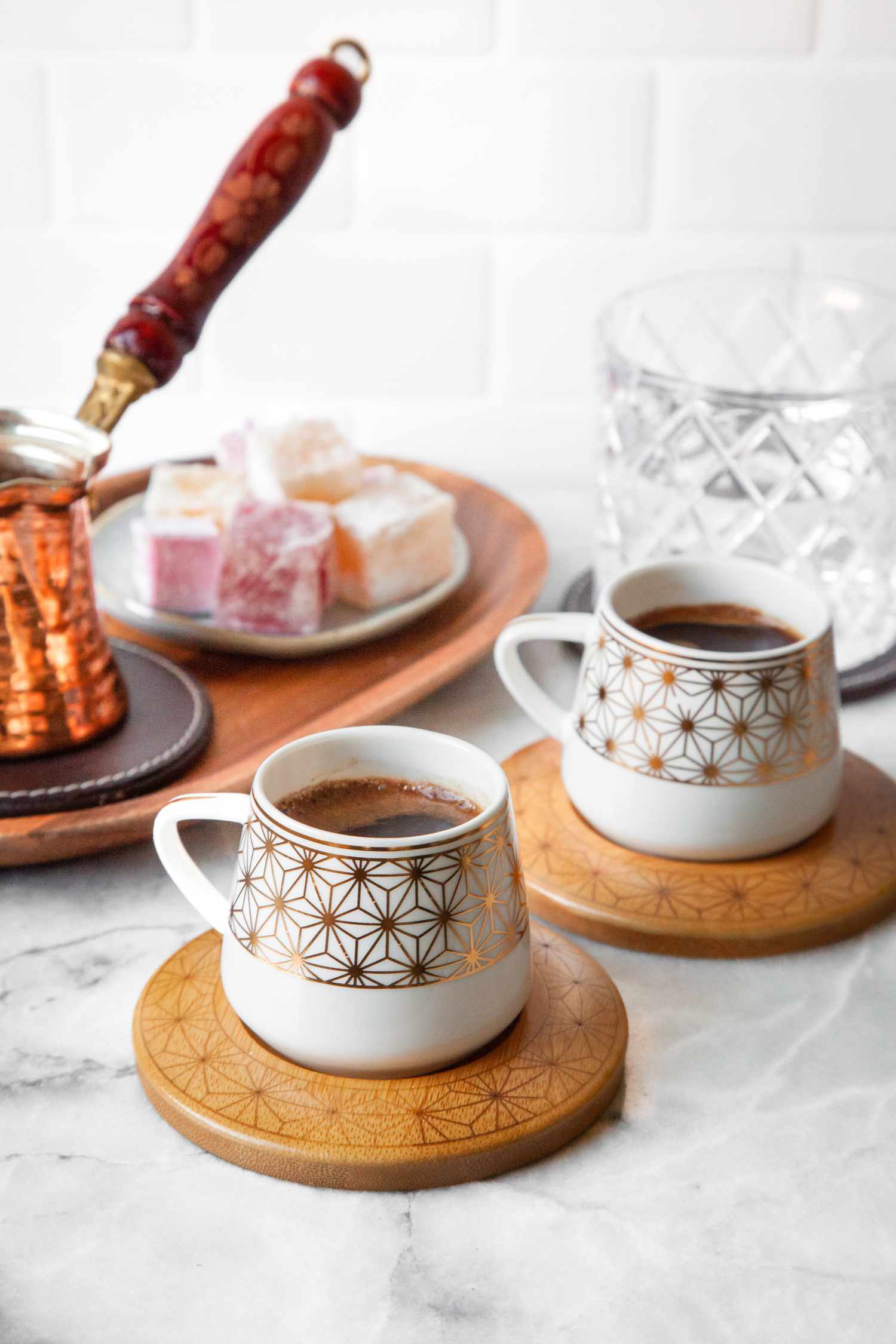 Two Cups of Turkish Coffee on Coasters, and in the Background, a Tray with a Cezve and a Small Plate of Turkish Delight