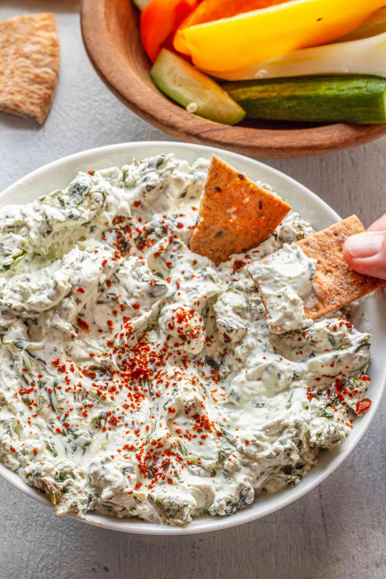Cracker Dipped into a Bowl of Easy Spinach Dip, Next to Another Bowl of Veggie Strips