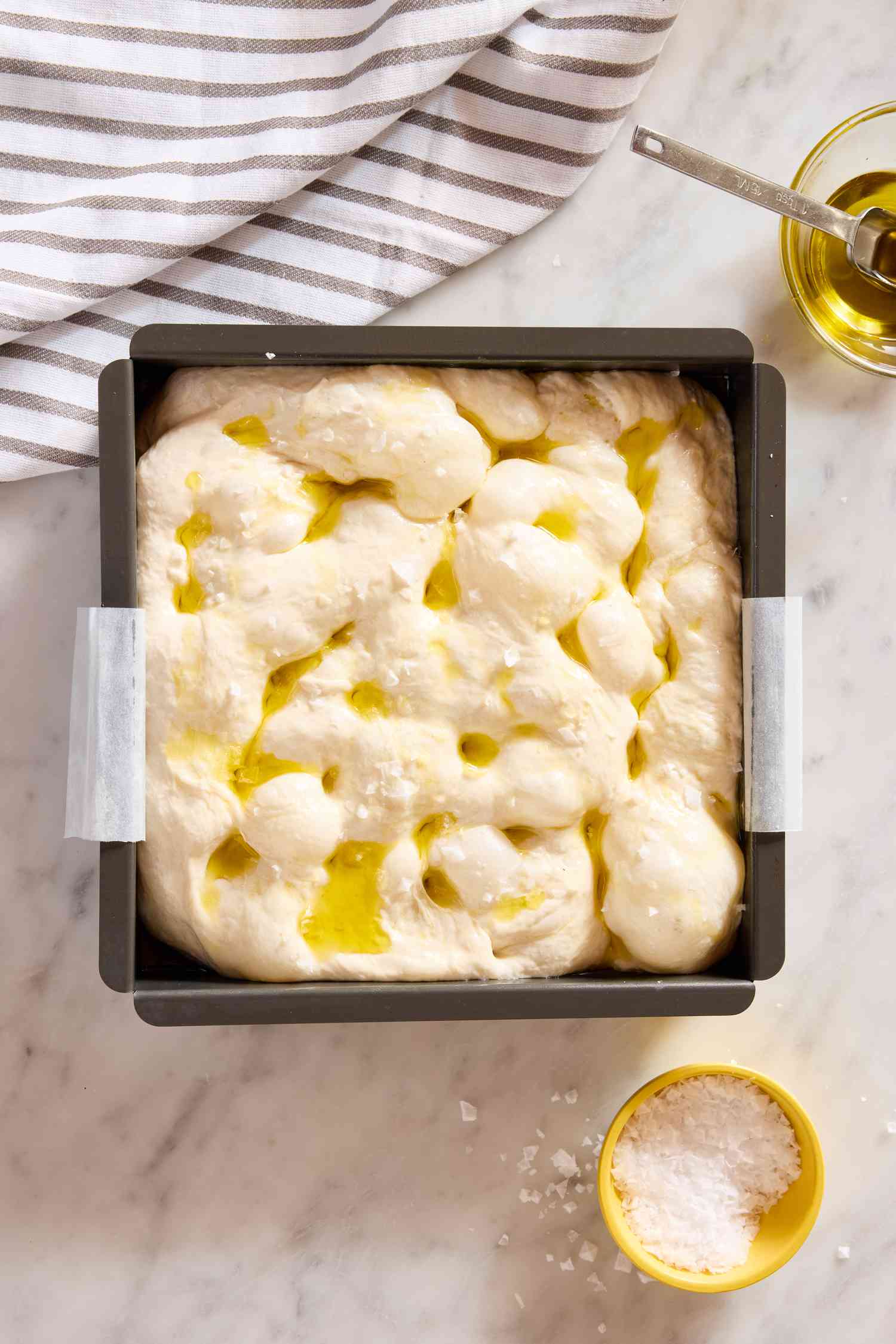 focaccia dough in a square pan, olive oil and salt on the side for King Arthur Flour’s Big and Bubbly Focaccia