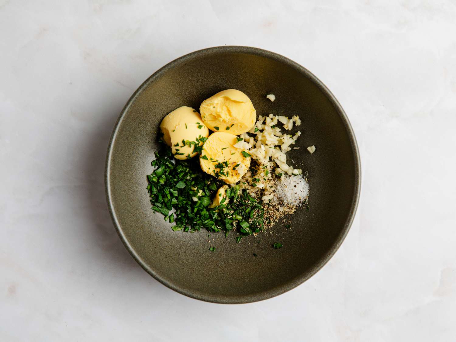 View from above of a bowl with egg yolks, chopped herbs, minced garlic, salt and pepper