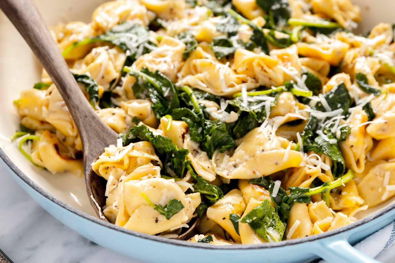 Close Up of Skillet Cacio e Pepe Tortellini With Wilted Greens in a Pot With a Wooden Serving Spoon