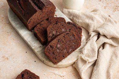 On a Marble Slab, Slices of Chocolate Banana Bread Next to the Rest of the Loaf, and on the Counter, a Glass of Milk, a Kitchen Towel, and a Slice of Bread