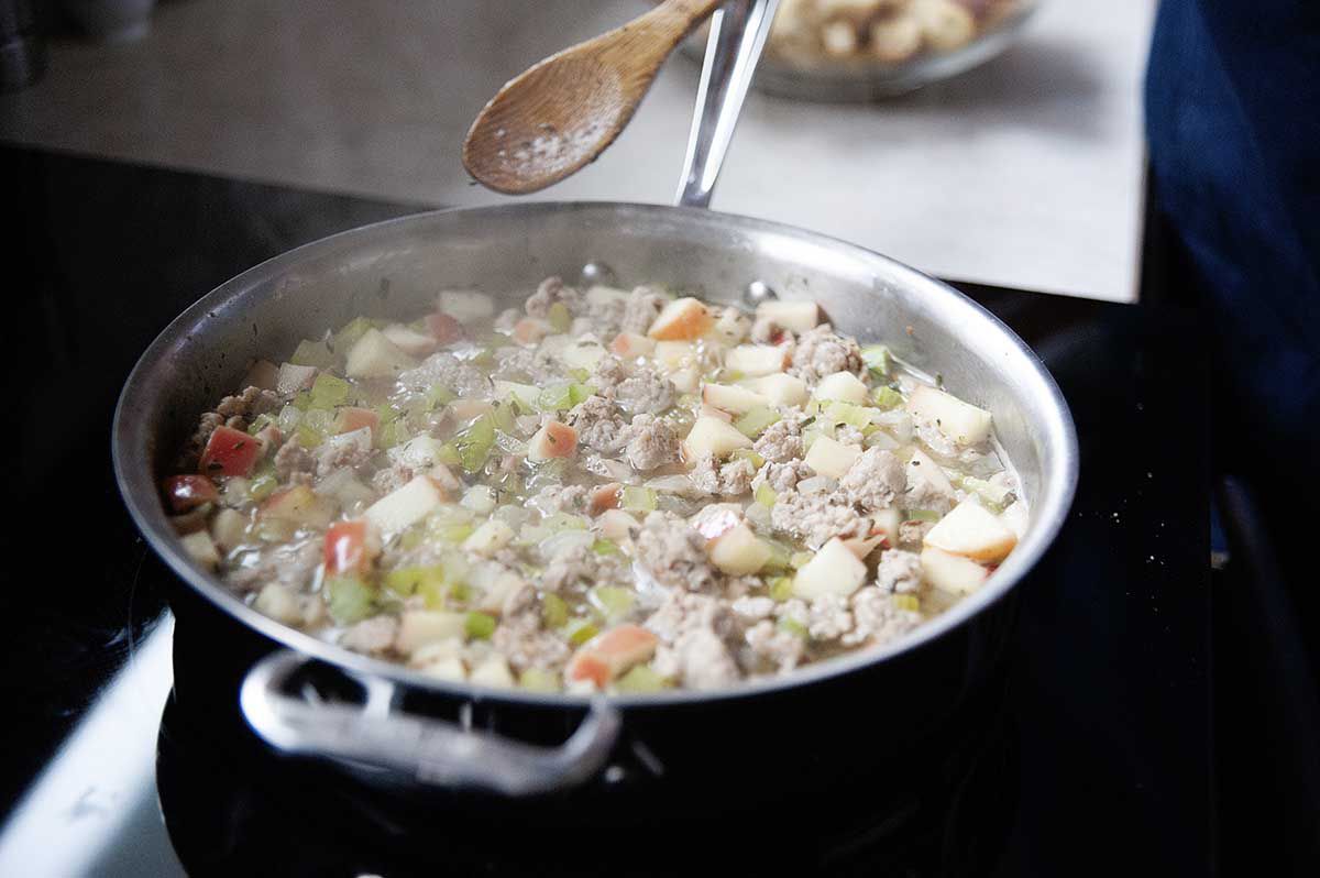 Woman simmering stock, pork and aromatics on the stovetop for the best Thanksgiving stuffing.