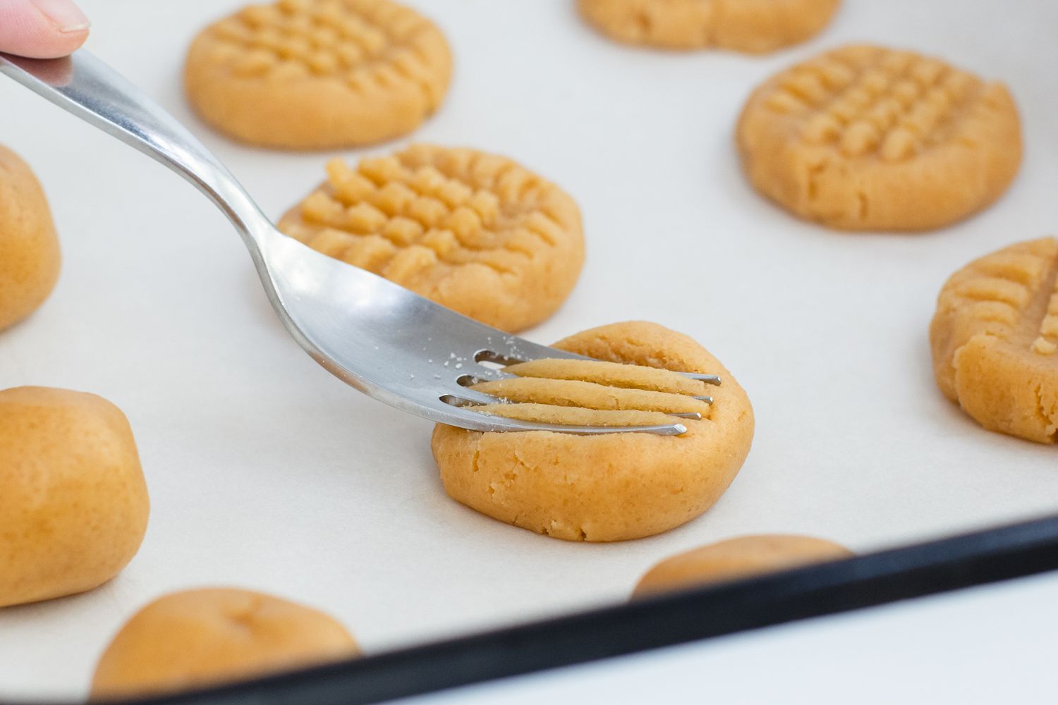 Pressing a fork in a crosshatch pattern on Peanut Butter Cookies.