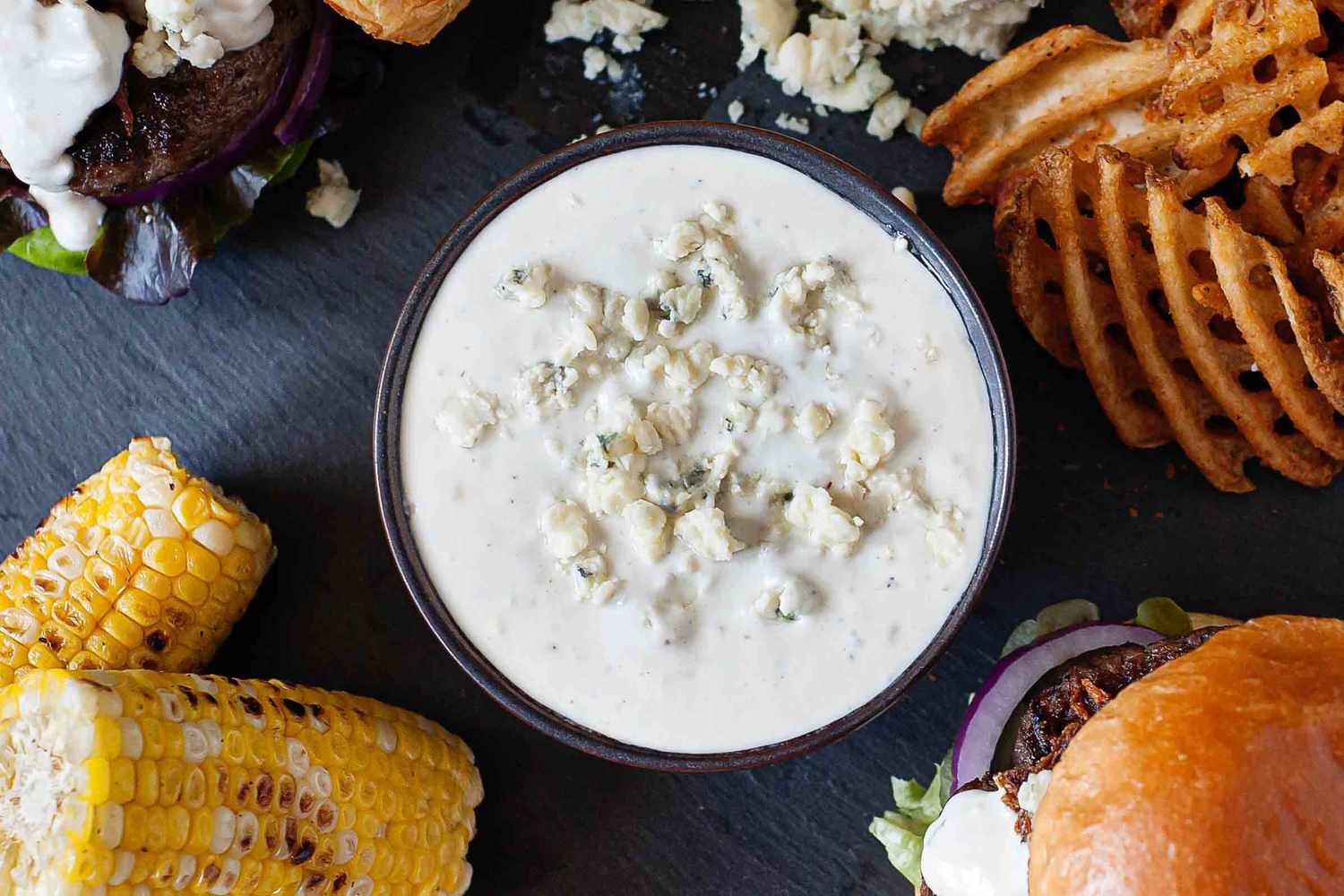 A bowl of blue cheese sauce surrounded by burgers and fries, ready for dipping.