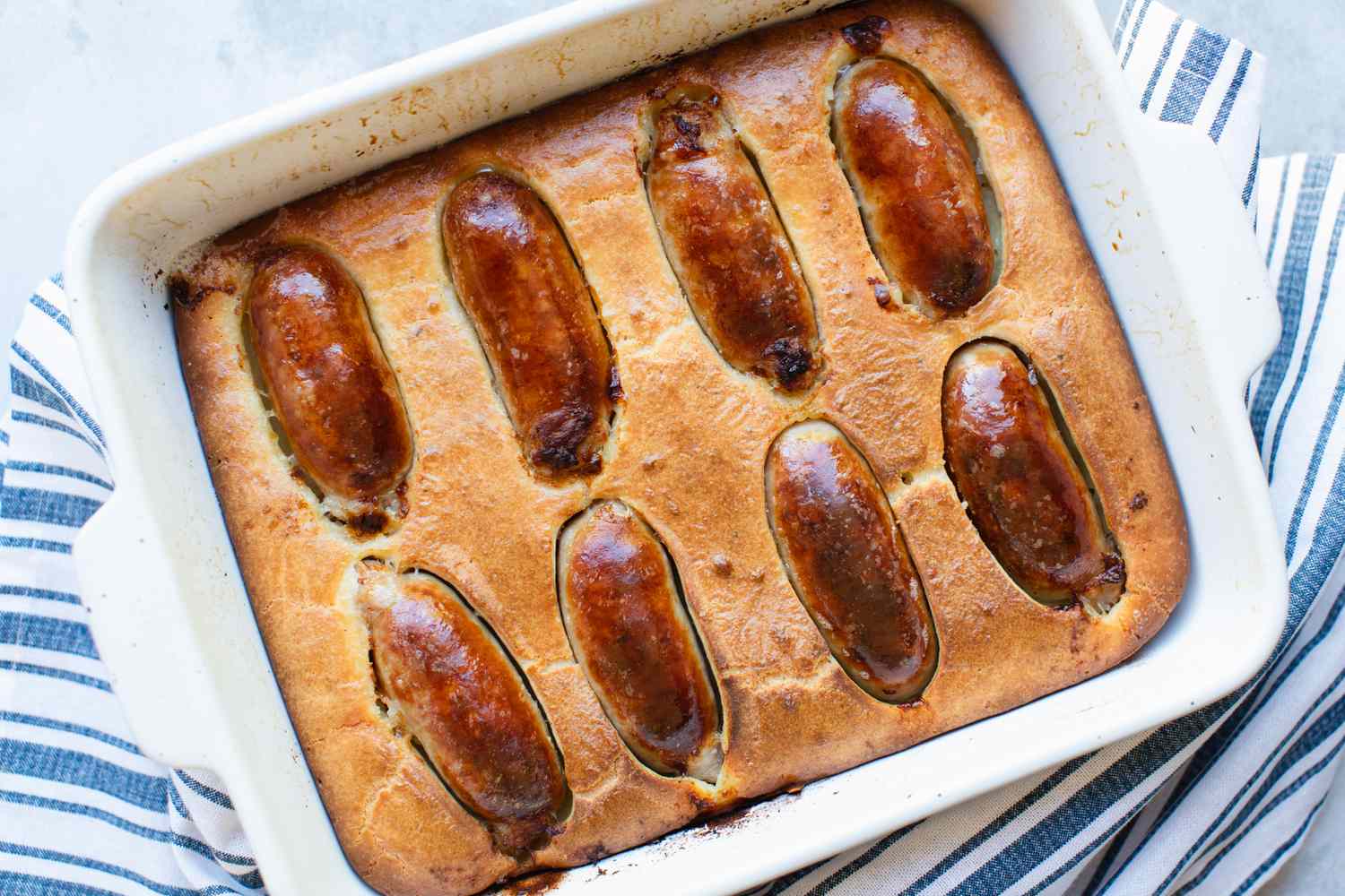Overhead view of toad in the hole in a baking dish with a blue striped linen underneath.