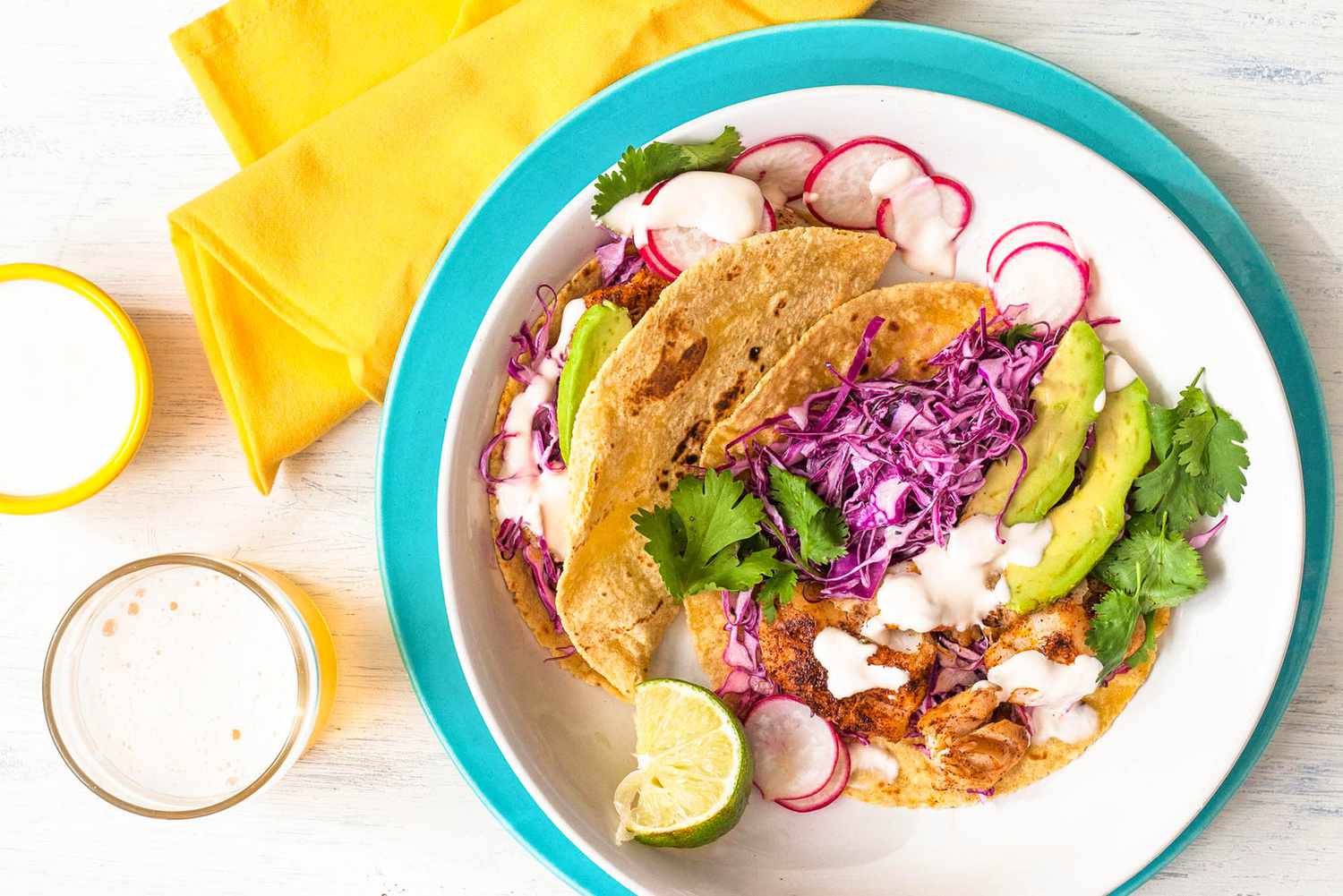 Overhead of fish tacos on a white an blue plate topped with avocado, cabbage, and cilantro 