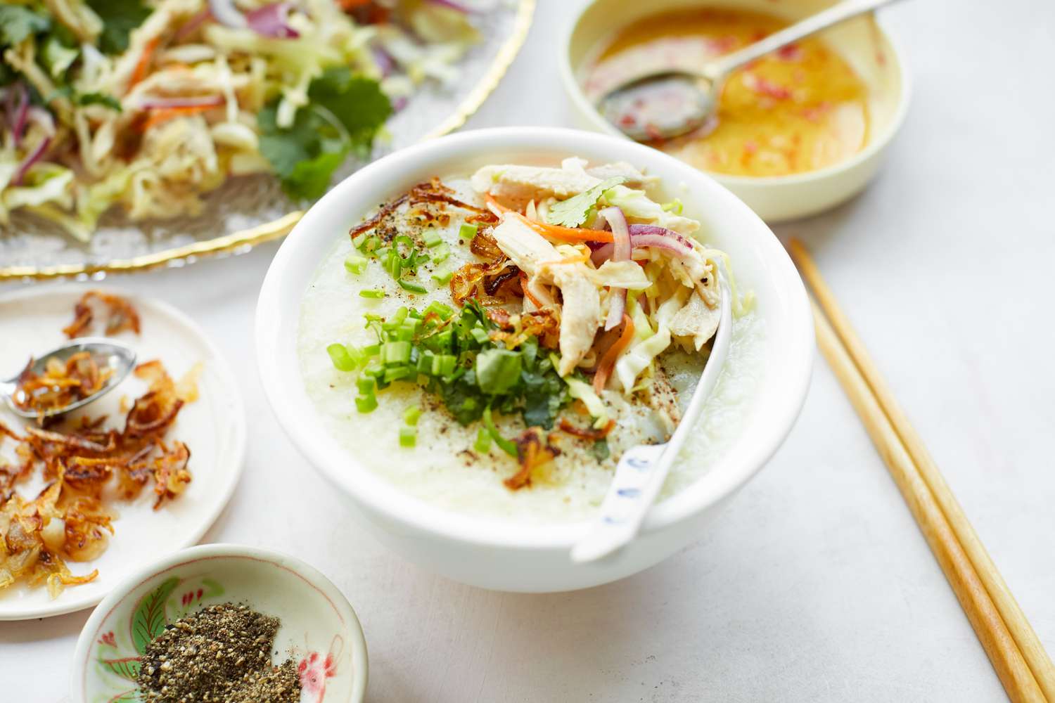 Chào Gá (Vietnamese Rice Porridge) in a Bowl Surrounded by Platter of Vegetables and Bowl of Sauce