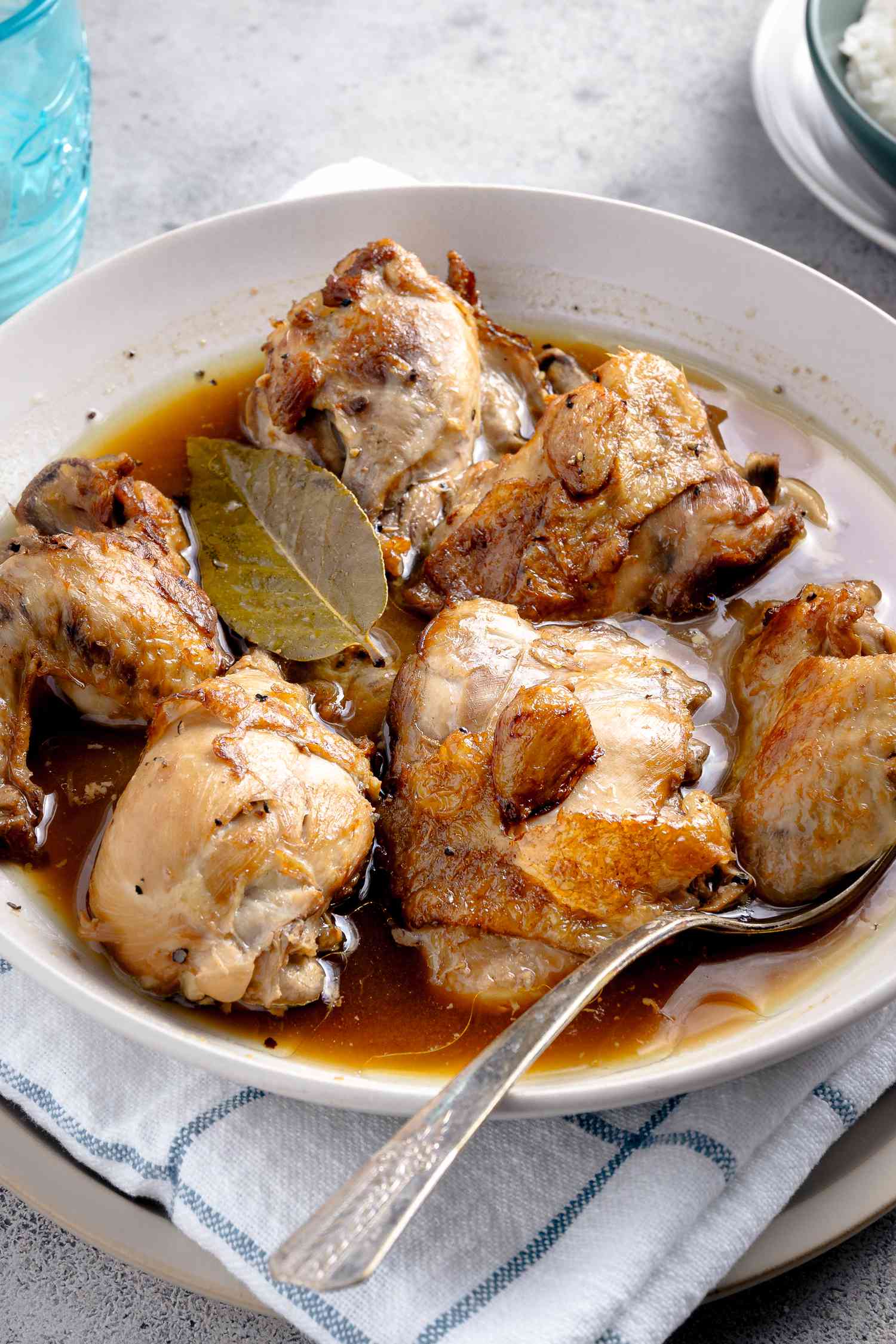 Chicken Adobo in a Bowl With a Spoon, and Under the Bowl, a Kitchen Towel