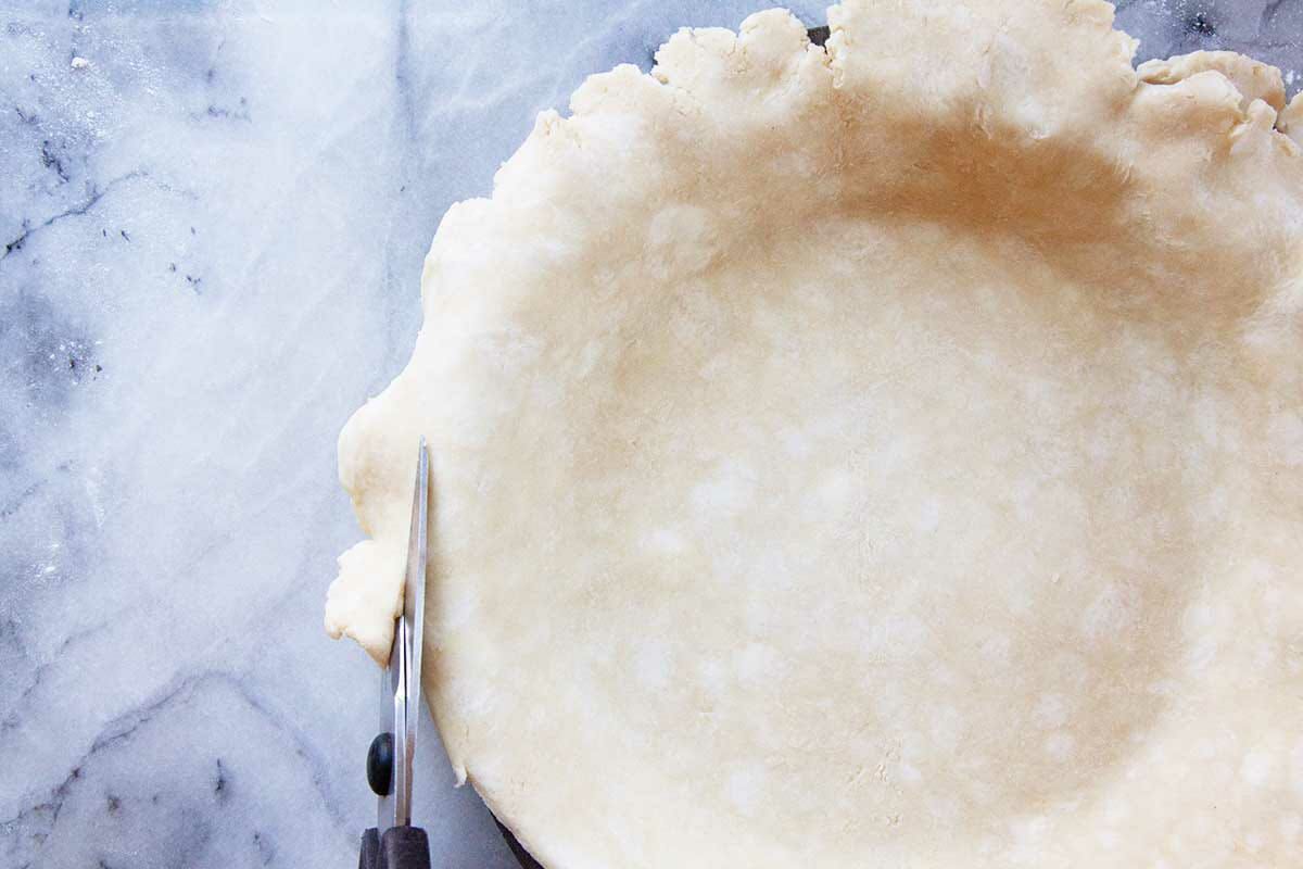 Trimming a pie crust with scissors to show how to make shoofly pie.