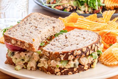 Side view of chickpea salad sandwich on a plate with chips.
