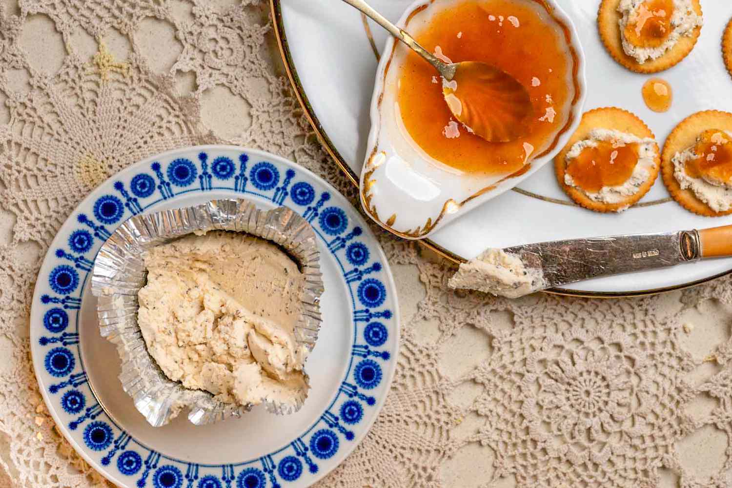 Overhead view of a small plate of Boursin cheese next to a large plate with a cheese knife, bowl of mango chutney and Ritz crackers topped with Boursin cheese and mango chutney all on an elaborate woven surface (Ami's 3-Ingredient Appetizer)