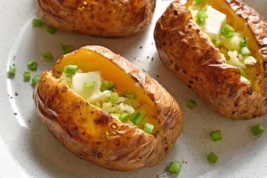 Baked potato on a plate topped with sliced onions and butter