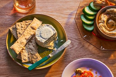 A plate with Boursin cheese and crackers, surrounded by a glass of wine, hummus and cucumbers