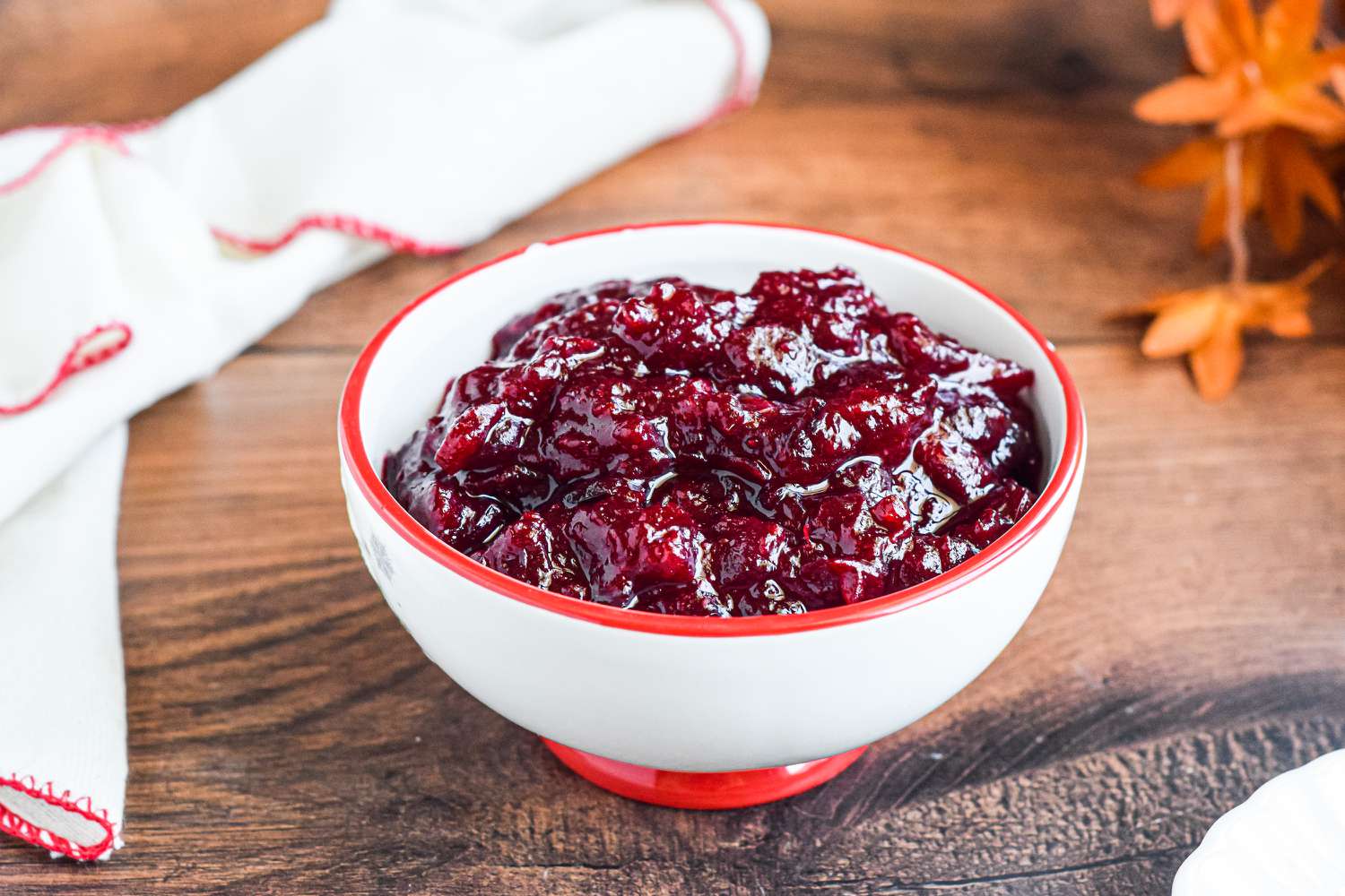 A white and red bowl of cranberry sauce on a table with a spoon.