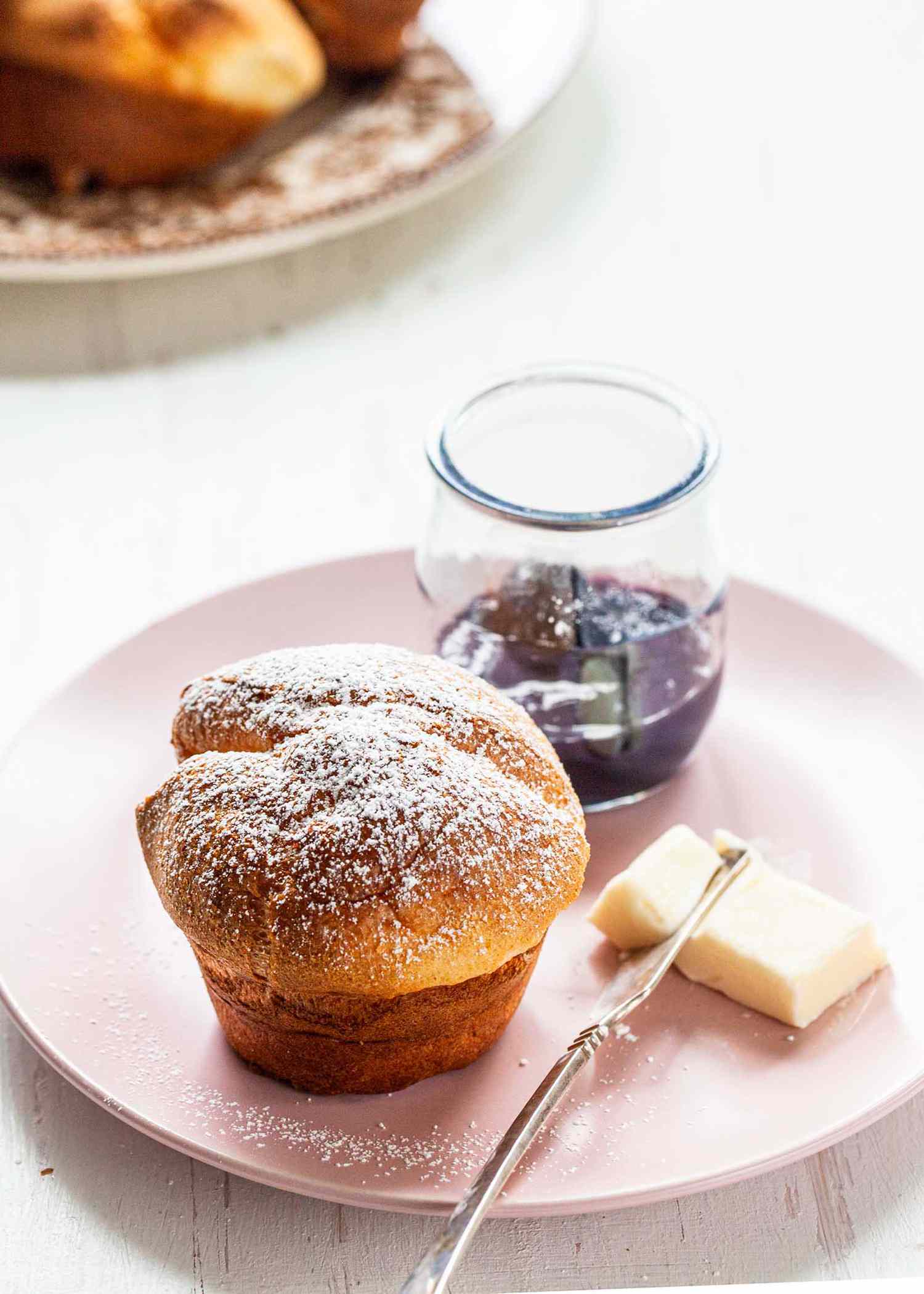 A popover on a plate with a pat of butter and jelly jar.