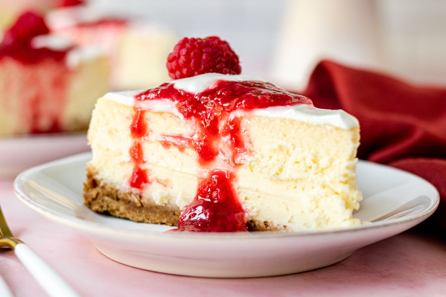 A slice of New York cheesecake on a plate topped with raspberry sauce.