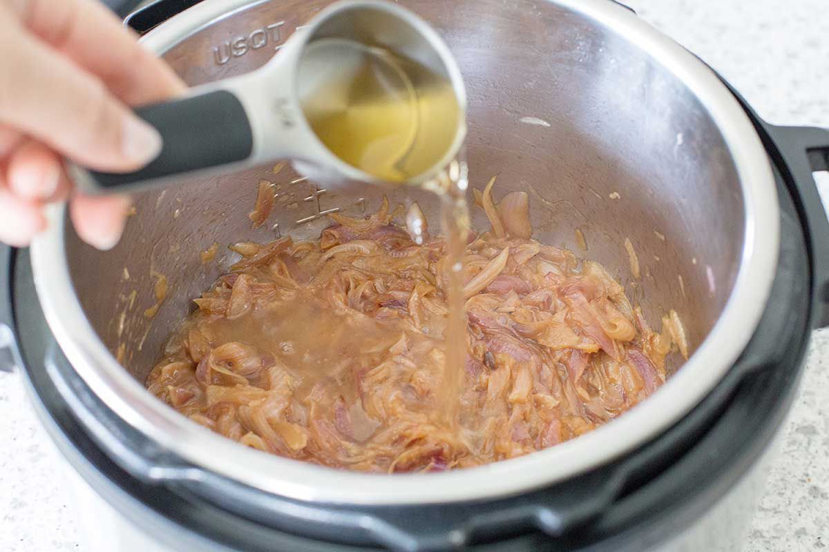 Adding broth to Simple Instant Pot French Onion Soup inside the metal bowl of an Instant Pot.