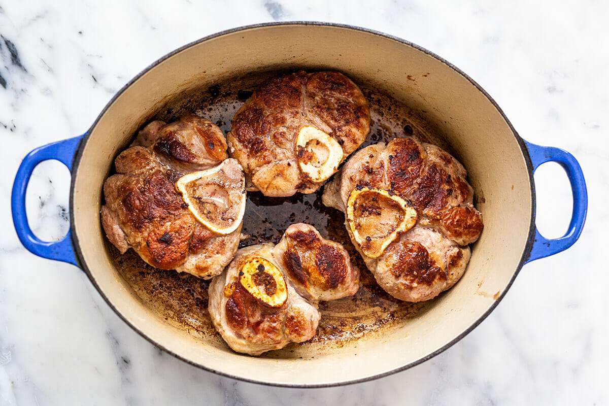 Dutch oven with meat for osso buco cooking inside.
