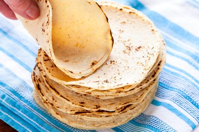 Corn tortilla recipe with corn tortillas stacked on a blue striped linen.