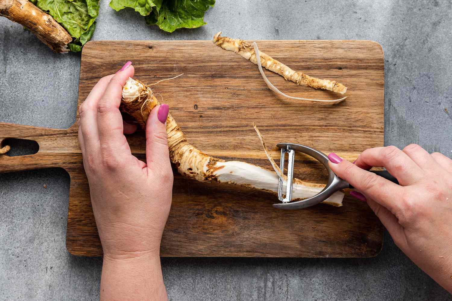 Hands Peeling a Raw Horseradish root with a peeler over a cutting board