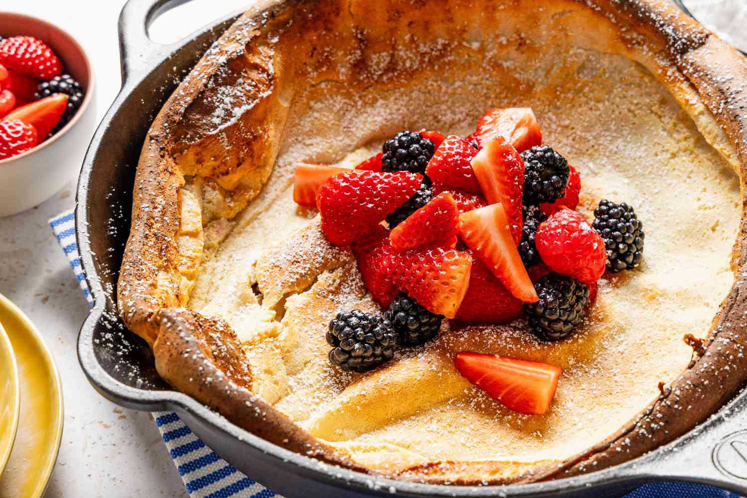 Dutch baby pancake topped with fresh strawberries, raspberries, and blackberries in a cast iron skillet