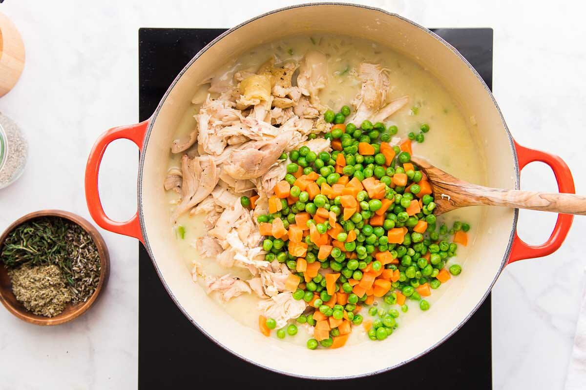 A dutch oven filled with shredded chicken, broth, peas and carrots to make a homemade Chicken Pot Pie.