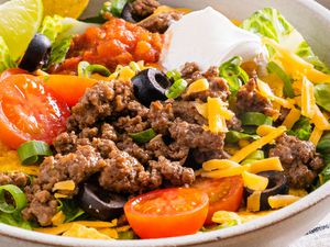 A bowl of taco salad garnished with sliced black olives and sour cream