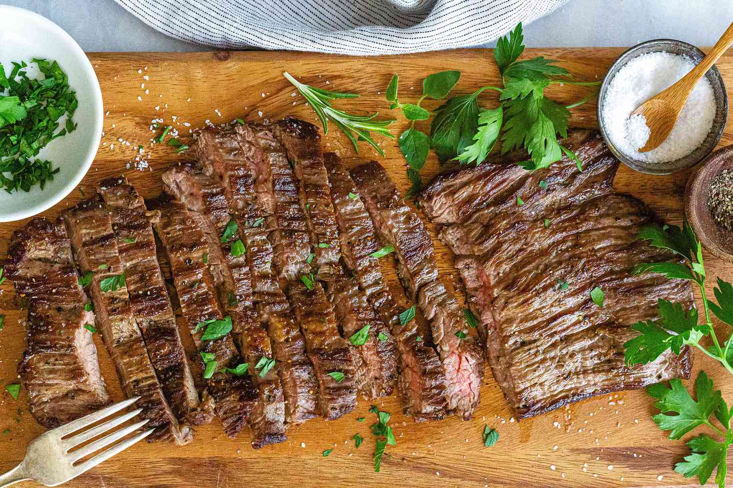 Sliced skirt steak on a wooden cutting board with herbs