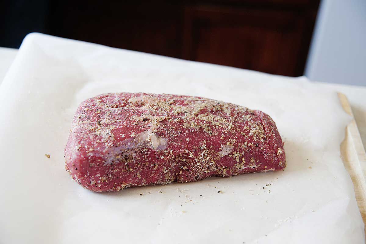 A roast on a cutting board covered in spices.