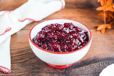 A bowl of cranberry sauce on a table with a spoon.