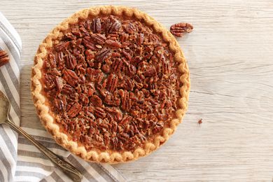 Overhead view of a pecan pie next to a striped towel and pie server all on a wooden tabletop