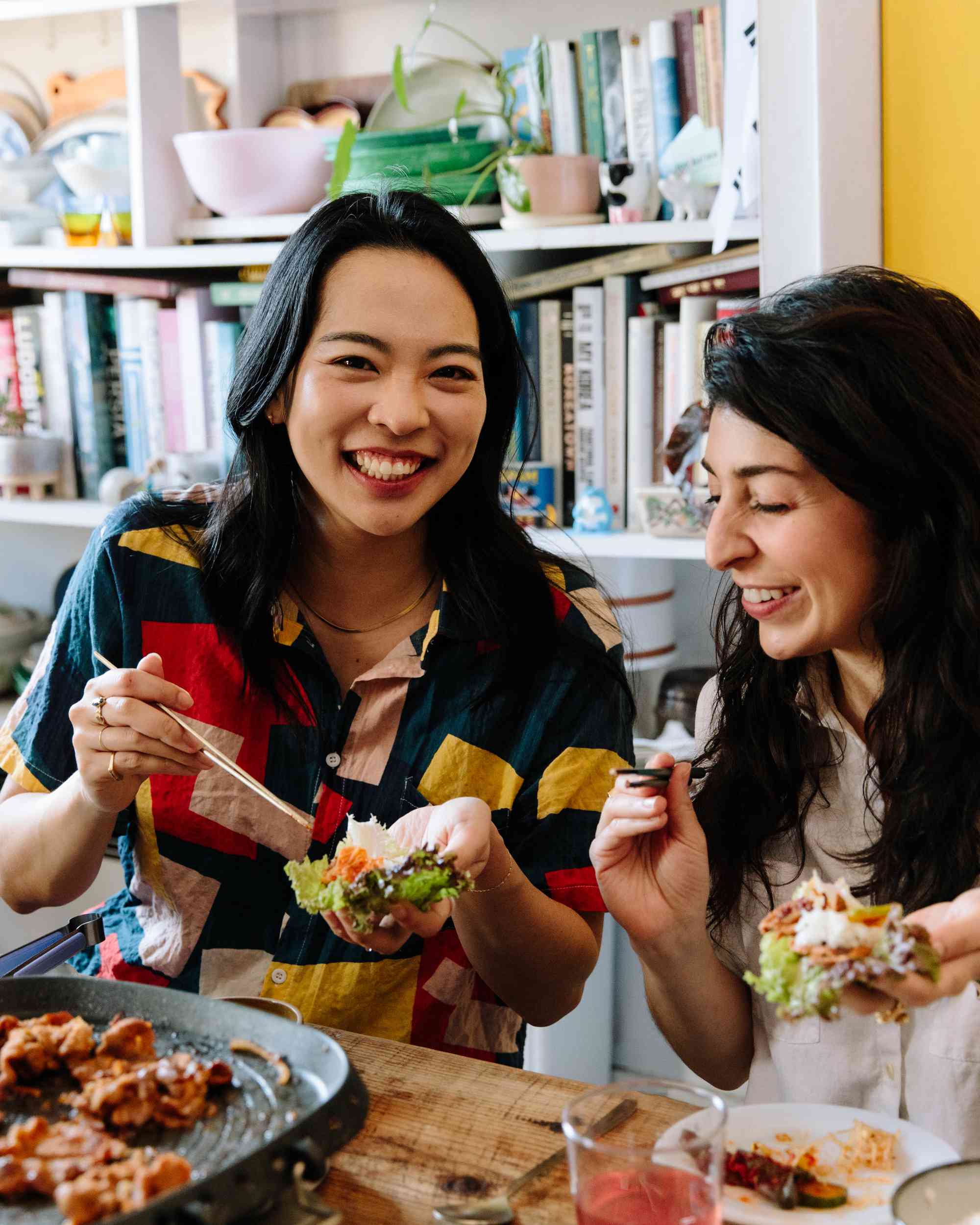 Two women enjoying Korean BBQ at a home table indoors. 