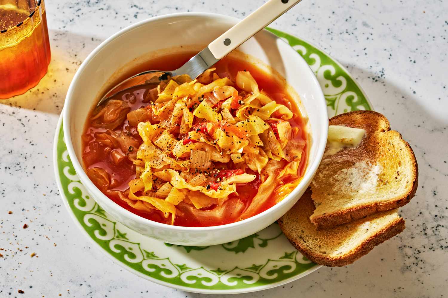 A serving bowl of cabbage soup on a plate with buttered toast on the side