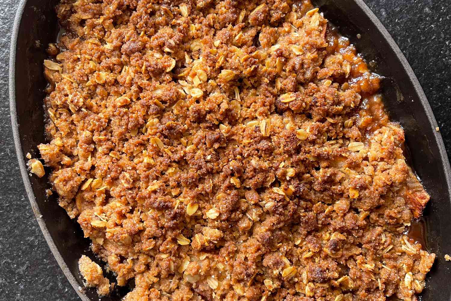 Close up of the apple crisp, showing a browned oaty topping and caramelized apple juices around the edge of the baking dish
