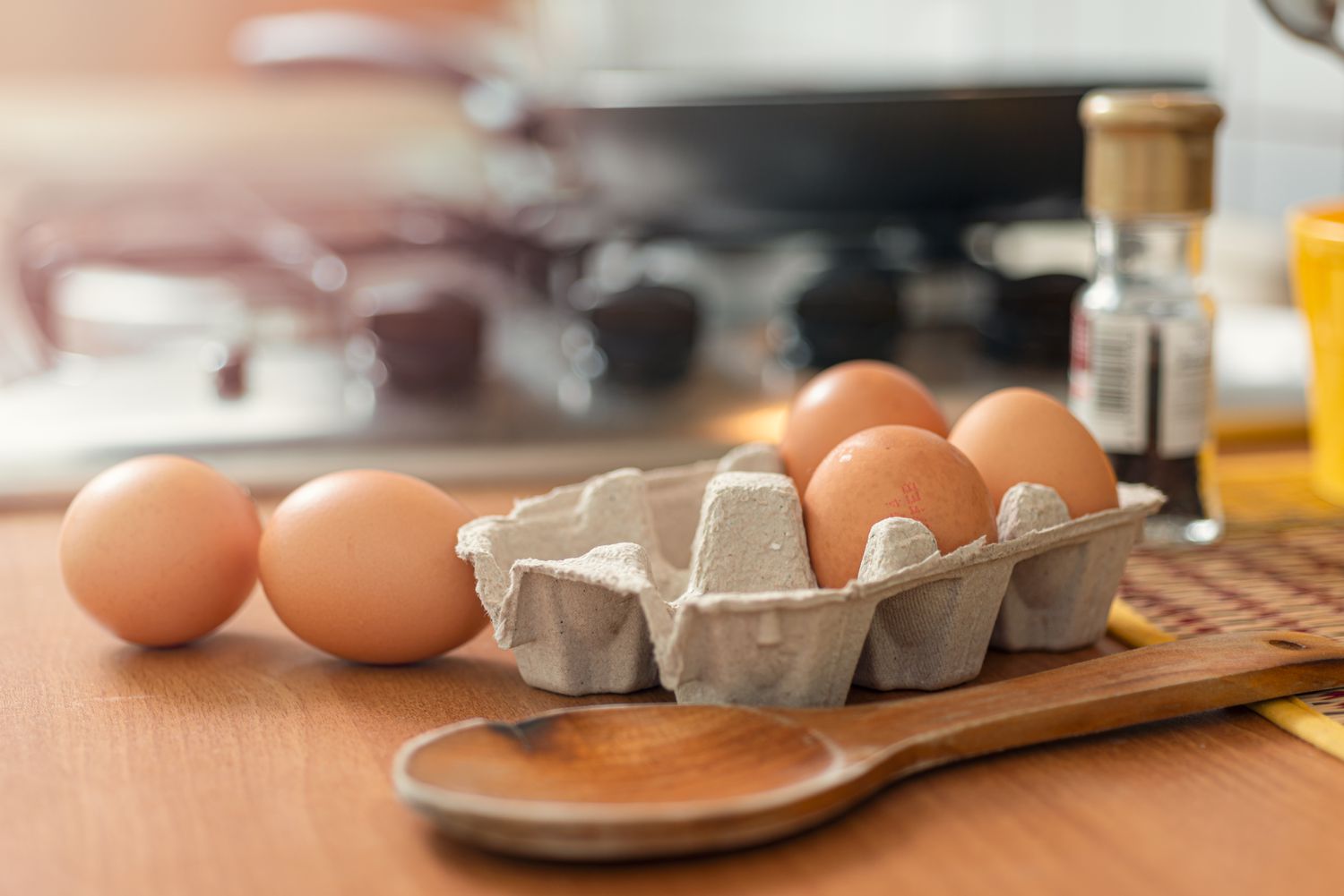 Brown eggs in an egg carton on a wooden kitchen counter next to a gas stovetop