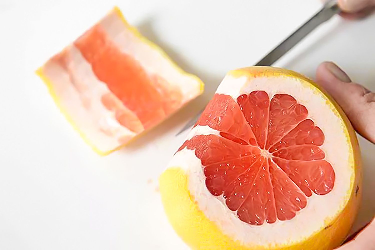 A Hand Holding a Citrus Fruit While the Other Hand Cuts Off the Peel (From One Pole to the Other) Using a Knife