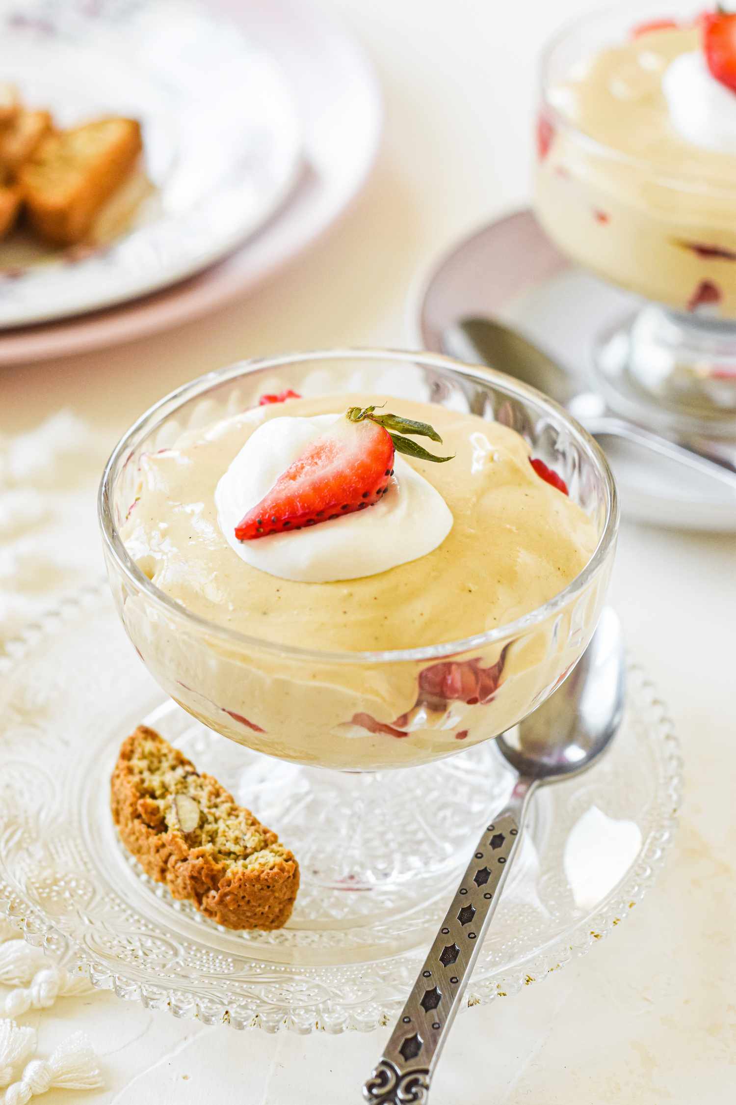 A parfait glass with sabayon sauce topped with cream and a strawberry.
