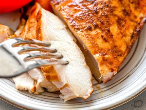 A fork tucking into slices of grilled chicken breast on a plate
