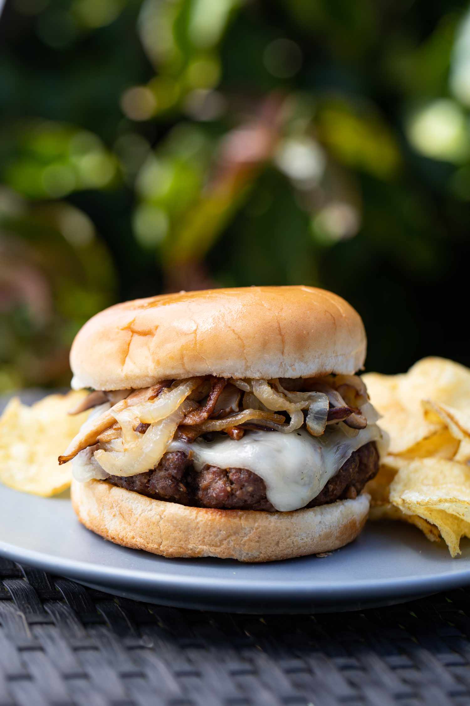 Side view of a mushroom and swiss burger on a plate with chips outside.
