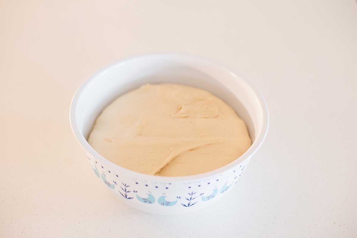The best beignet dough is rising in a white bowl on a counter.